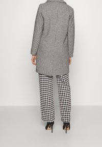 Abrigo de pata de gallo en blanco y negro combinado con pantalones a juego de pata de gallo, con un diseño ajustado y zapatos de tacón alto.