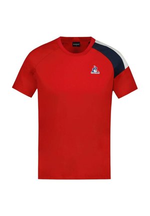 Camiseta roja de manga corta con cuello redondo, que presenta un acento azul y blanco en el hombro y un logo en el pecho. Textura de tela suave.