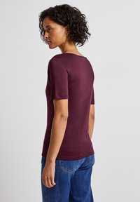 Burgundské tričko s krátkým rukávem, kulatým výstřihem, slim fit a hladkou texturou, doplněné modrými džíny v neformálním stylu.