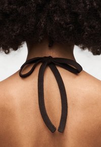 Καφέ υφαντή κορδέλα δένει στο πίσω μέρος ενός γυμνού ώμου, αναδεικνύοντας την υφή του δέρματος και τα απαλά σγουρά μαλλιά από πάνω.