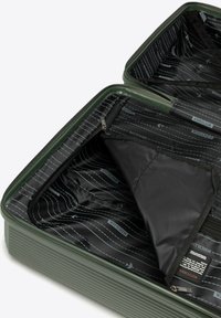 Grüner Hartschalenkoffer mit gerippter Oberfläche, ausgestattet mit einem schwarzen gemusterten Innenraum. Beinhaltet Reißverschlussfächer und Netzsäcke zur Organisation.