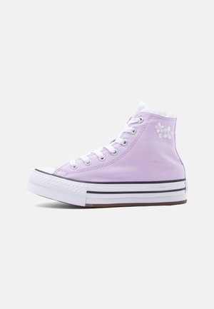 Baskets montantes en toile lavande avec lacets blancs, semelle blanche épaisse à rayures noires et petite broderie florale près de la cheville.