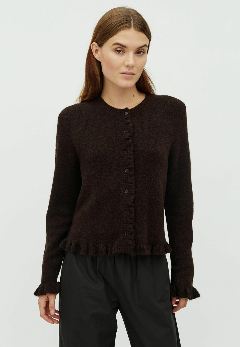 Barna, kötött kardigán kerek nyakkivágással, elöl gombos záródással és fodros részletekkel az alján és az ujjaknál. Puha anyag és testhez álló fazon.