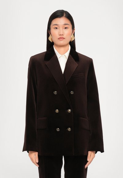 Blazer en velours marron à double boutonnage, avec des revers en pointe, des boutons dorés, des poches latérales et une silhouette structurée.