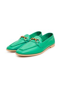 Par grønne læder loafers med brune såler og dekorative gyldne og brune metalspænder på hvid baggrund.
