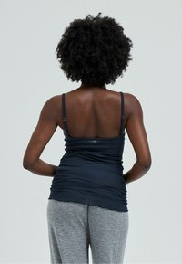 Canottiera blu navy con spalline regolabili e texture arricciata. L'orlo inferiore è ondulato, abbinata a pantaloni sportivi grigi in morbido cotone.