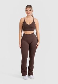 Bruin sportief set bestaande uit een aansluitende cropped top met verstelbare bandjes en hooggetailleerde legging, beide gemaakt van een gestructureerd, rekbaar materiaal.