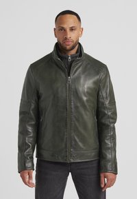 Lederjacke in Dunkelgrün mit Stehkragen, Reißverschluss vorne und Seitentaschen. Glatte Textur mit dezentem Schimmer und minimalistischer Gestaltung.