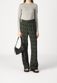 Woman wearing a gray long-sleeve top, patterned wide-leg pants, black sandals, and holding a black handbag with a chain strap.