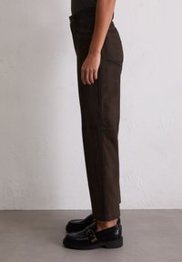 Helle braune Wildleder-Hosen mit hoher Taille und geradem Bein. Verfügt über Seitentaschen und sichtbare Nähte, kombiniert mit schwarzen Mokassins.