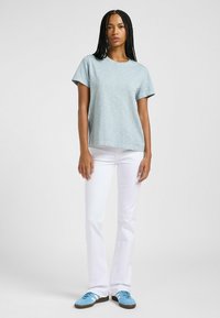 T-shirt azzurro chiaro a maniche corte in tessuto morbido, abbinato a pantaloni bianchi a campana e sneakers blu. Design minimal con una texture delicata.
