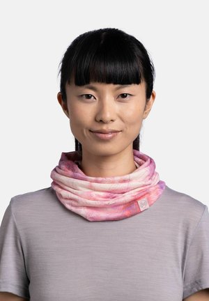 Mujer con cabello negro que lleva un pasamontañas de cuello rosa y morado con patrón y una camiseta de manga corta lila claro, mirando hacia adelante, fondo neutro.