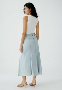Een lichtblauwe denimrok heeft een uitlopende snit met voornaad en een rafelige zoom, gedragen met een witte mouwloze top en tan hakken.