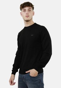 Pullover nero a maniche lunghe con colletto rotondo e polsini a costine. Presenta un piccolo logo sul petto. Realizzato in un tessuto morbido e leggero.