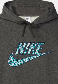 Grå hoodie lavet af en blanding af bomuldsstof har et stort blå og hvidt spraglet Nike-logo på forsiden, med sorte snore i hætten.