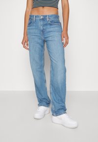 Ljusblå denimjeans med rak benform, femfickorsdesign och kontrasterande sömmar. Matchas med vita sneakers.