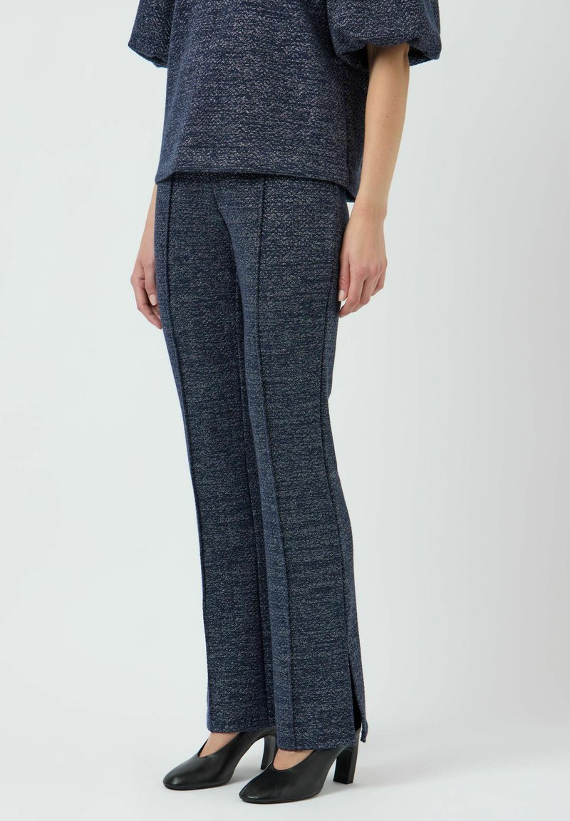 Completo in maglia testurizzata blu navy composto da pantaloni a gamba larga con spacchi laterali, abbinato a una maglietta dal taglio ampio, stilizzato con scarpe con tacco nere.