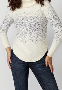Maglione a collo alto color crema con un motivo testurizzato, caratterizzato da macchie blu. Tessuto morbido e lavorato a maglia con orlo curvo. Abbinato a jeans scuri.