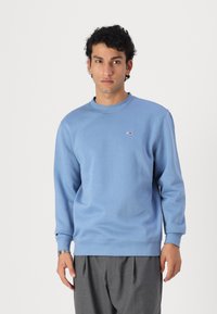 Sudadera azul clara con cuello redondo y mangas largas. Presenta un pequeño logotipo en el pecho, fabricada en suave material de algodón.