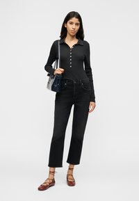 Svart langermet poloskjorte med knappet stolpe, kombinert med svarte jeans med rette ben, og røde flats med snøring. Modellen holder en mørk veske.