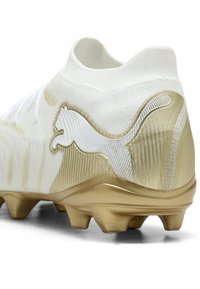 Άσπρο και χρυσό ποδοσφαιρικό παπούτσι με υφασμένη σόλα και εμφανές λογότυπο πούμα που φαίνεται σαν να πηδάει στη φτέρνα.