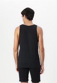 Top de tirantes negro sin mangas, con textura suave y escote redondo. Combinado con pantalones cortos negros a juego, que exhiben un diseño simple y minimalista.