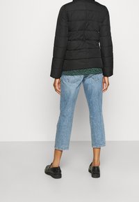 Chaqueta acolchada negra con costuras horizontales, llevada sobre una blusa de un patrón verde, combinada con jeans cortos de mezclilla azul claros y zapatos negros.