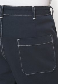 Pantalones azul marino con una tela texturizada, acentos de costura blanca y un bolsillo trasero con corte recto y costuras limpias.