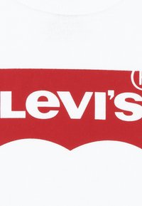 Vit bomulls-t-shirt med en stor röd Levi's-logotyp med tydlig vit text och en krökt design under logotypen. Mjuk textur.