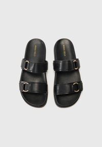 Black slide sandals made of textured synthetic material, featuring two wide straps with gold-tone circular hardware and a flat sole.