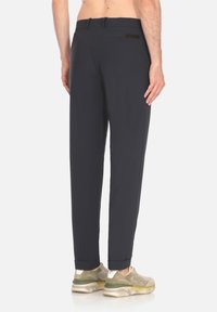 Pantaloni blu navy scuri con gambe affusolate e una texture liscia. Presentano un accento nero sulla tasca posteriore. Indossati con scarpe da ginnastica di colore chiaro.