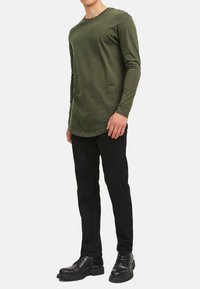 Oliven grøn langærmet skjorte med rund hals, parret med sorte slim-fit bukser og sorte snøring støvler. Glat tekstur, afslappet design.