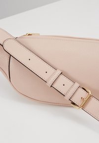 Sac en cuir rose avec une finition texturée, équipé d'une boucle en métal doré et d'une sangle ajustable. Forme lisse et incurvée avec des coutures visibles.