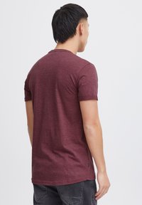 Burgunderfarbene Kurzarm-T-Shirt, figurbetontes Design, strukturierter Stoff, Rundhalsausschnitt, nahtlose Schultern, Rückansicht mit einem kleinen Markenetikett am Saum.