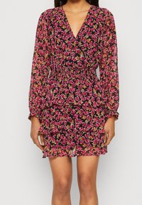 Blommig minikjol med svart bakgrund, genomskinligt tyg, djup V-ringning, långa ärmar, elastisk midja och lager av volangkant.