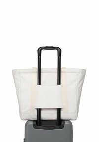 Valise rigide grise avec poignée noire étendue, sac fourre-tout crème attaché à la poignée par une sangle, fond blanc.