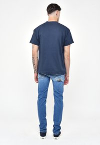 Námořnická modrá bavlněná tričko s krátkým rukávem, doplněné o světle modré džíny. Džíny mají výrazný trojúhelníkový design kapsy.