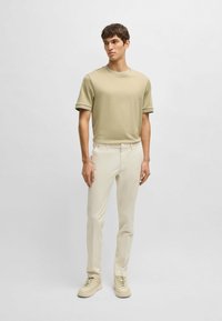 Maglietta verde chiaro a maniche corte abbinata a pantaloni slim-fit crema e sneakers beige, caratterizzata da una texture liscia e un design semplice.