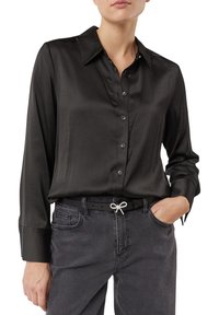 Czarna satynowa koszula na guziki z ostrym kołnierzykiem, długimi rękawami i gładką fakturą. Połączona z szarymi dżinsami i czarnym paskiem ozdobionym kokardką.