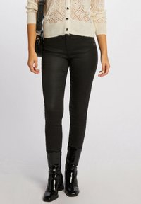 Jeans skinny neri in tessuto elasticizzato, con un design aderente. Abbinati a stivali neri in vernice al ginocchio per un look elegante.