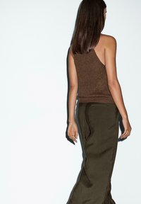 Top in maglia marrone con design a spalla singola, abbinato a pantaloni larghi color oliva, che mostrano un tessuto testurizzato e una vestibilità rilassata.