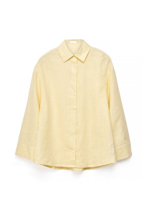 Valge taustal eksponeeritud helekollane pika varrukaga nööpidega särk, klassikalise kraega ja veidi lõdva istuvusega.