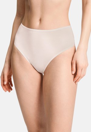 Vrouw draagt naadloos beige hoog getailleerd ondergoed, toont de middenpartij en de bovenbenen tegen een effen achtergrond.