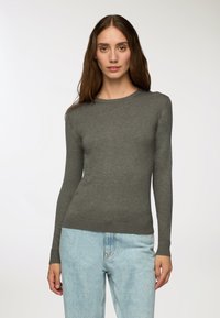 Szary sweter z długim rękawem, wykonany z delikatnego materiału, z okrągłym dekoltem i prążkowanymi mankietami. Noszony z jasnoniebieskimi spodniami o wysokim stan. 