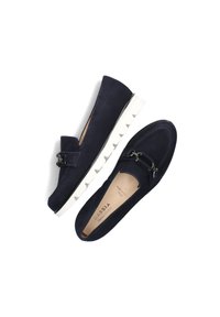 Marineblauwe suède loafers met een witte geribbelde zool en een decoratief gespsymbool. Glad textuur, ronde vorm en instapontwerp.