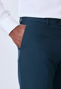 Námořnické modré texturované kalhoty s boční kapsou, doplněné bílou košilí s dlouhým rukávem. Mají zapínání na knoflík a poutka na opasek.