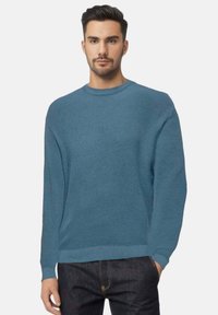 Maglione blu lavorato a maglia con scollo rotondo e maniche lunghe. Presenta una vestibilità comoda e polsini a coste, abbinato a jeans in denim scuro.