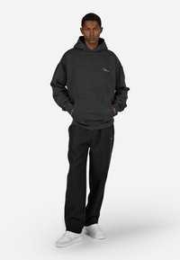Czarna bluza z kapturem z kieszenią kangurką i małym haftowanym logo. W połączeniu z luźnymi czarnymi spodniami i białymi trampkami. Gładka tekstura.