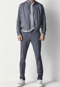 Szara kurtka bombowca z wysokim kołnierzem, biała swetrowa koszulka o fakturze, dopasowane szare spodnie i białe trampki. Gładki materiał, minimalistyczny design.