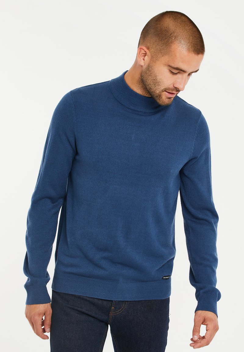 Kobaltblauer gestrickter Pullover mit einem hohen, gerippten Kragen, langen Ärmeln und einem geraden Saum, der ein kleines Logotag am unteren Rand aufweist.